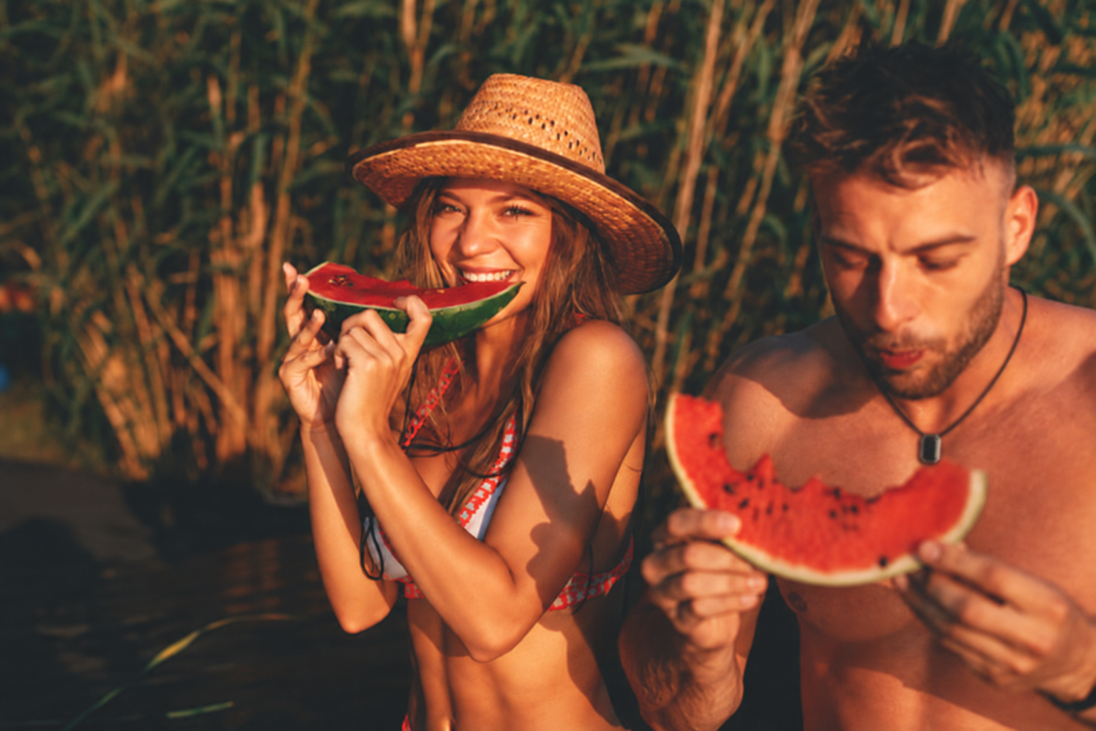 Two people eating watermelon at sunset, one wearing the ORIN pendant.