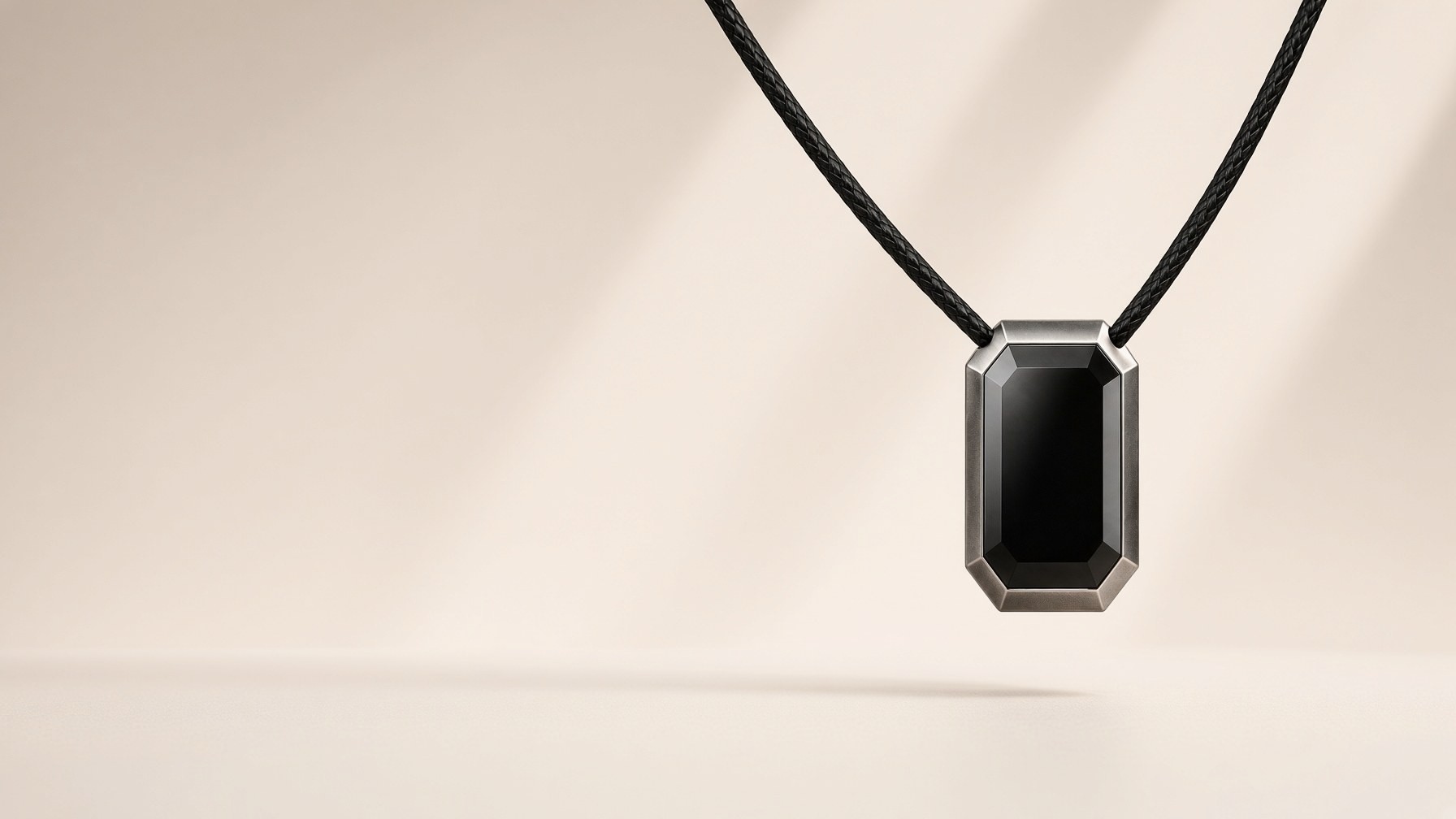 ORIN pendant, a small black faceted jewel in a brushed metal frame on a black braided cord.